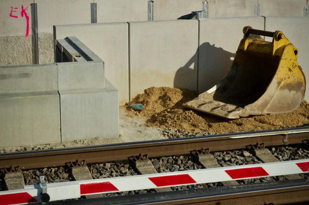 Close-up view of a railway construction site featuring a large yellow excavator bucket next to tracks.
