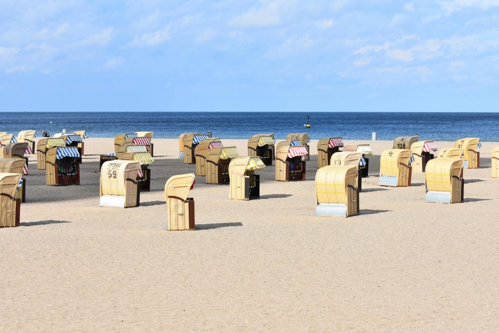 Serene beach scene with rows of empty wicker beach chairs under a blue sky.